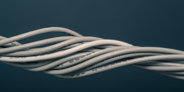 Close-up image of multiple intertwined white and gray cables against a dark blue background.